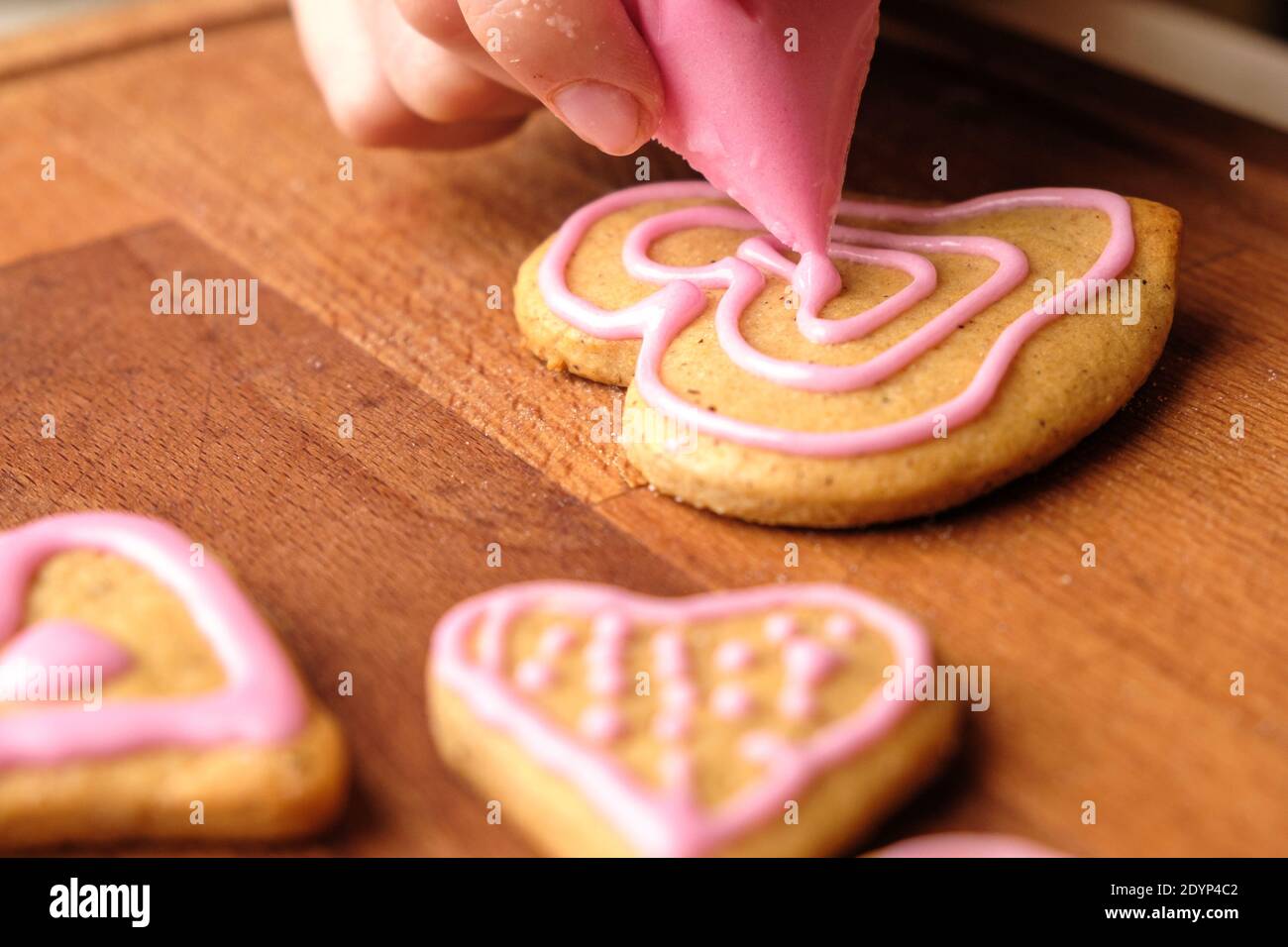 Das Sahnehäubchen des Valentinstag. Frau Dekoration Lebkuchen in Form von Herzen auf einem Holztisch. Stockfoto