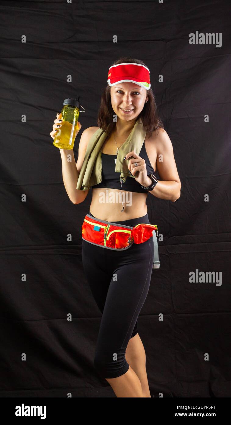 Schönes Mädchen in Jogging rote Uniform, trinkt Wasser nach dem Training im Studio auf schwarzem Hintergrund. Stockfoto