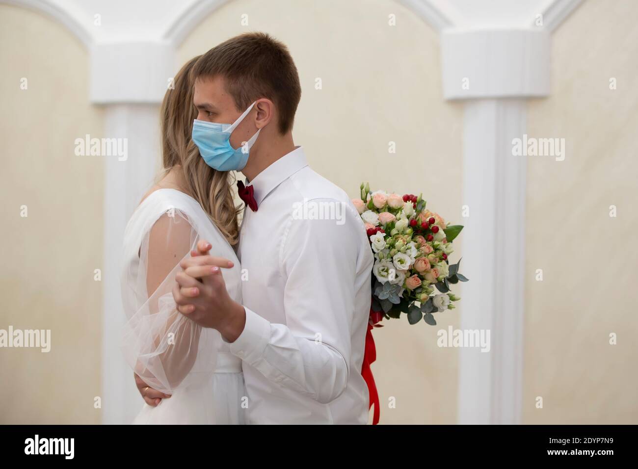 Die Braut in einer medizinischen Maske mit einem Blumenstrauß tanzt mit dem Bräutigam. Hochzeit während der Coronavirus panademia. Stockfoto