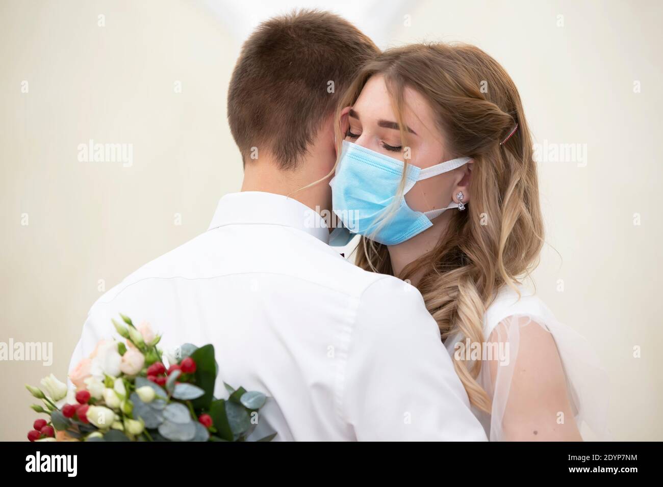 Die Braut in einer medizinischen Maske mit einem Blumenstrauß tanzt mit dem Bräutigam. Hochzeit während der Coronavirus panademia. Stockfoto