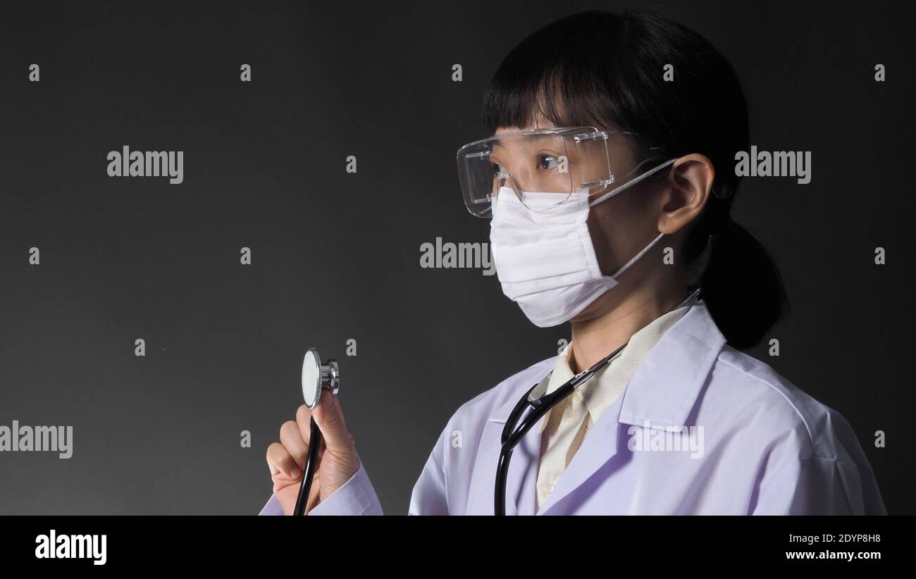 Arzt trägt medizinische Maske und klare Brille oder Brille und Stethoskop am Hals und weiße Uniform. Asiatische Ärztin oder Wissenschaftlerin im Schutz Stockfoto