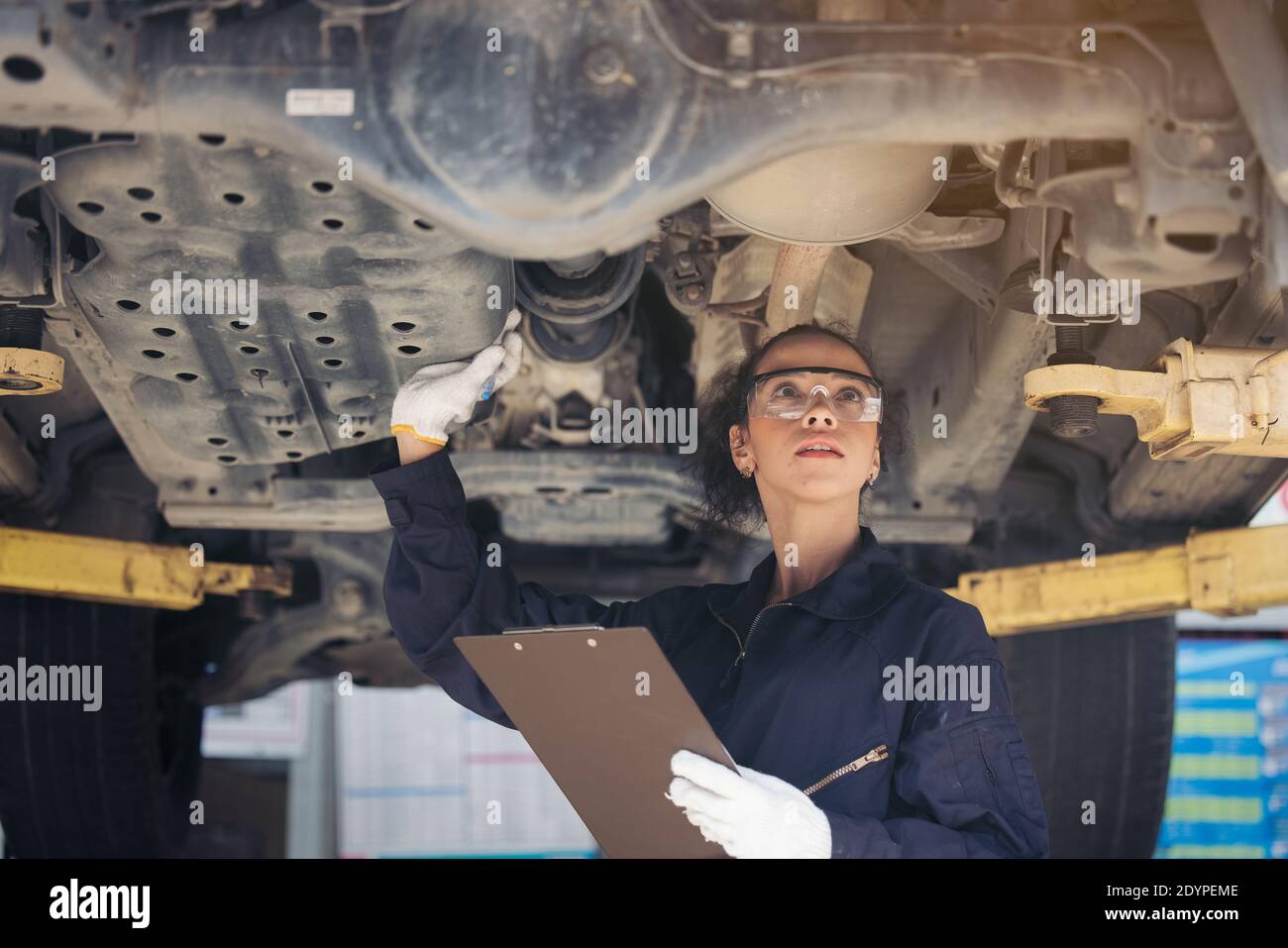 Weibliche Mechanikerin, die ein angehobener Wagen inspiziert Stockfoto