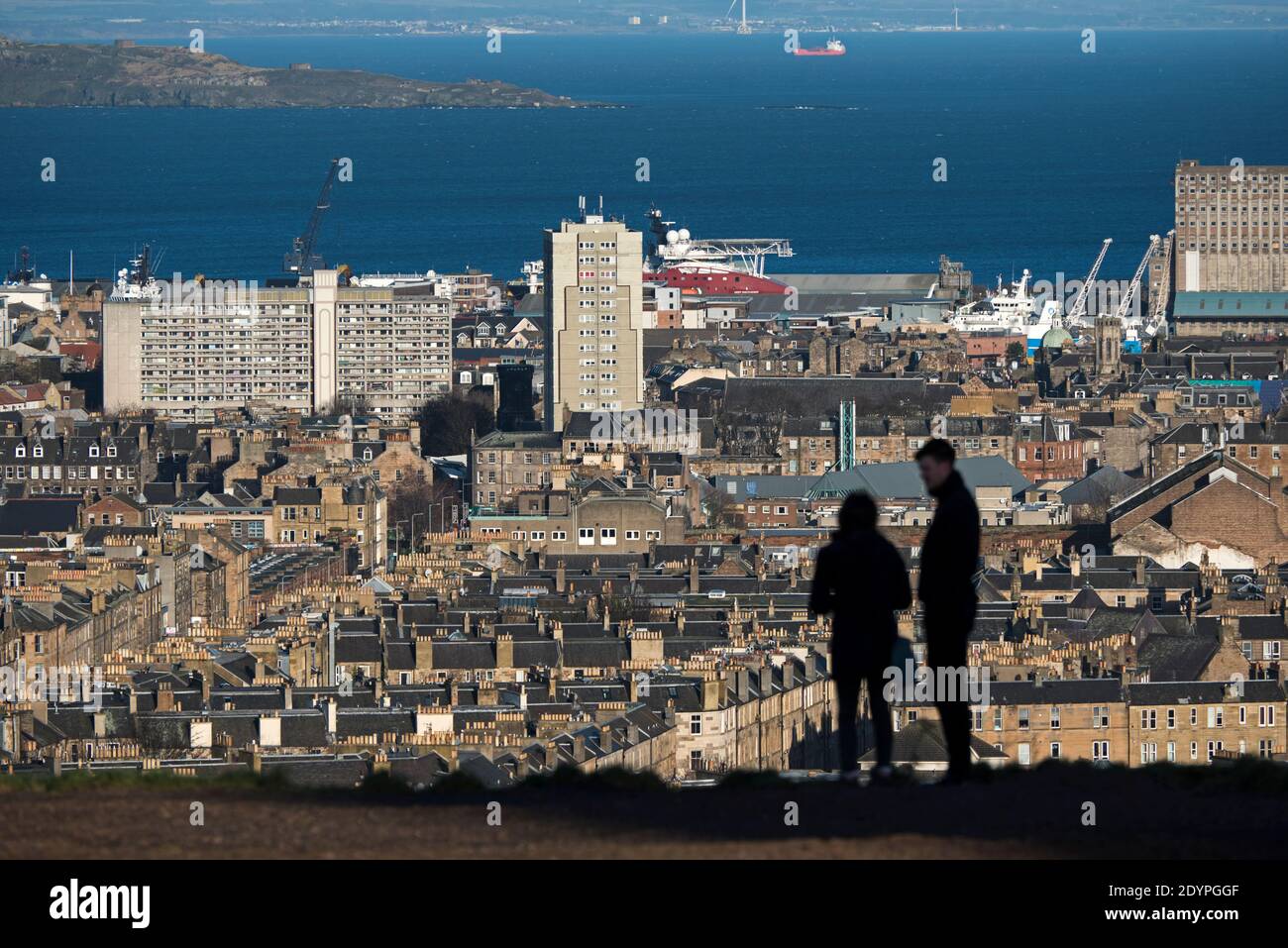Die Silhouette eines Paares, das auf Calton Hill steht und nach Norden in Richtung Leith und Firth of Forth in Edinburgh, Schottland, Großbritannien schaut. Stockfoto
