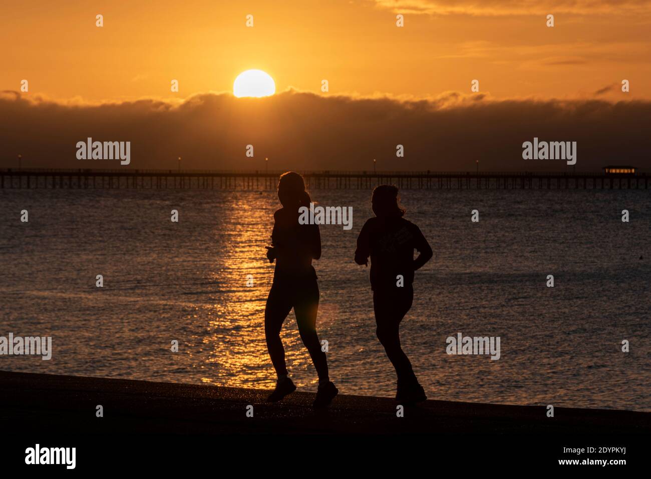 Jogginginnen, die an der Strandpromenade bei Sonnenaufgang am Weihnachtstag in Southend on Sea, Essex, Großbritannien, laufen. Läufer joggen im Morgengrauen Stockfoto