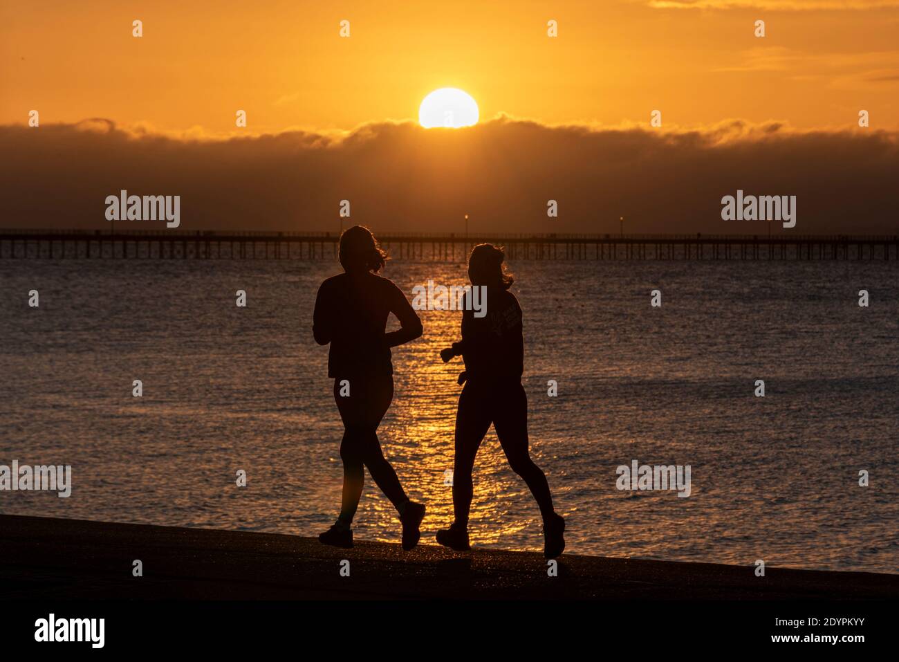 Jogginginnen, die an der Strandpromenade bei Sonnenaufgang am Weihnachtstag in Southend on Sea, Essex, Großbritannien, laufen. Läufer joggen im Morgengrauen Stockfoto