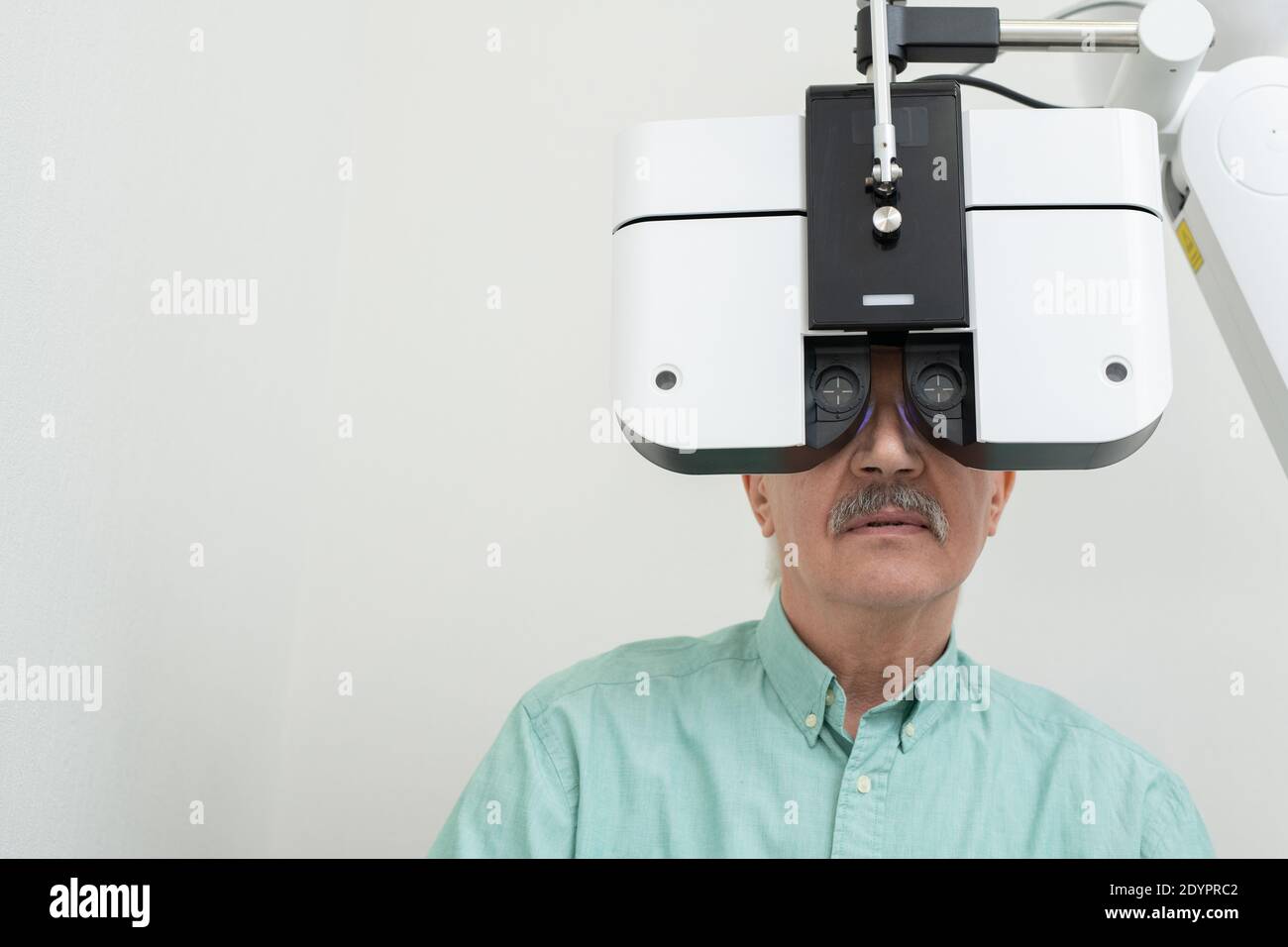 Älterer männlicher Patient, der vor ophthalmologischen Geräten sitzt und Blick durch das Objektiv, während seine Sehkraft in überprüft Kliniken Stockfoto