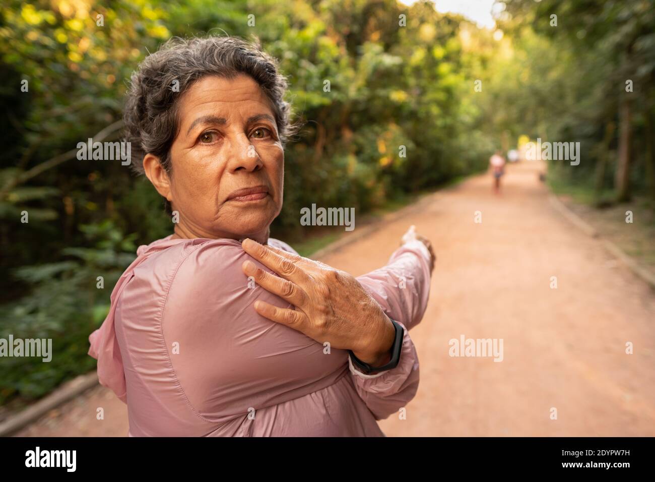 Ältere gemischte Rasse Frau Blick auf Kamera und strecken die Arme. Im Freien in grüner Umgebung. Überwinden, gesund, Fitness, Frische-Konzept. Stockfoto