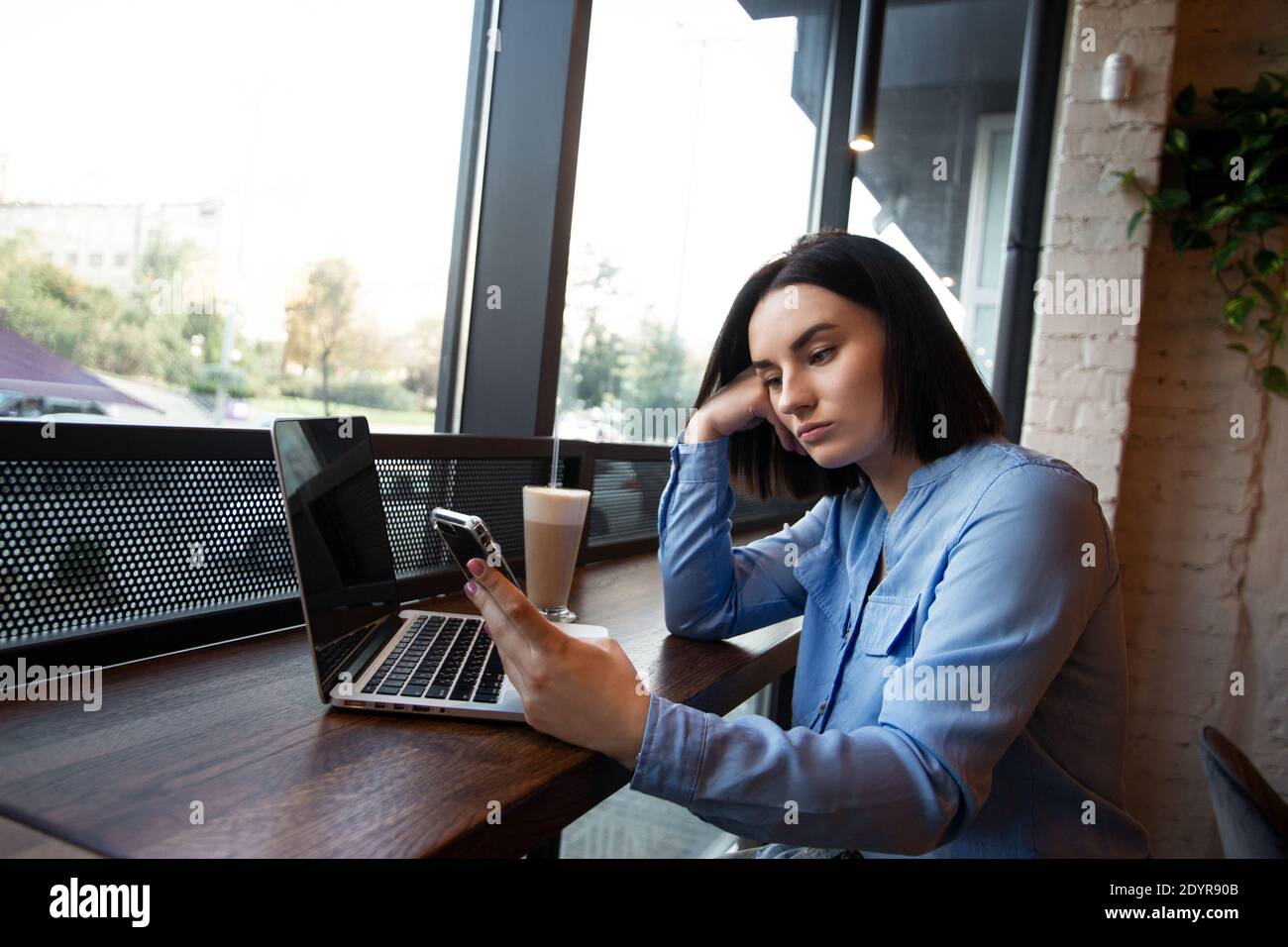 Müde Freiberuflerin, die im Café arbeitet. Konzept der Konzentrationsprobleme. Verärgert junge Frau suchen in Smartphone und wartet auf einen Anruf. Gemütlicher Kaffee Stockfoto
