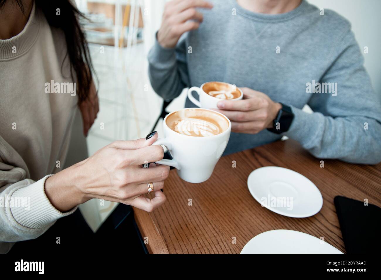 Junges Paar trinkt heiße Getränke. Nahaufnahme Frau und Mann sitzen im Café und halten warme Tassen Kaffee auf dem Tisch. Mann und Frau verbringen Wochenende in Stockfoto