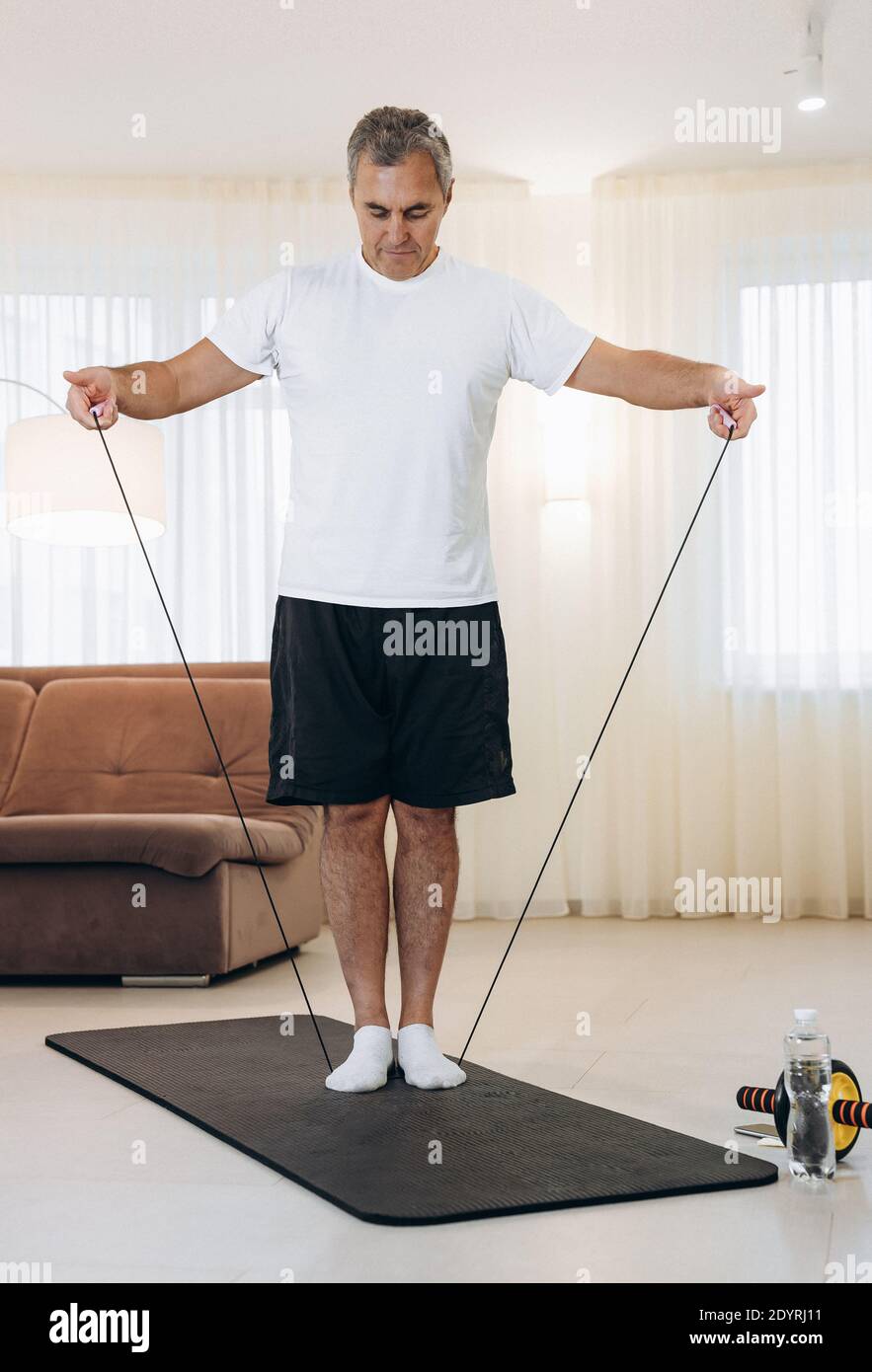 Der ältere Mann führt Übungen mit einem Widerstandsband durch. Wohlbefinden und Aktivität im Alter Konzept. Mann macht Handübungen zu Hause. Starker Mann Stockfoto