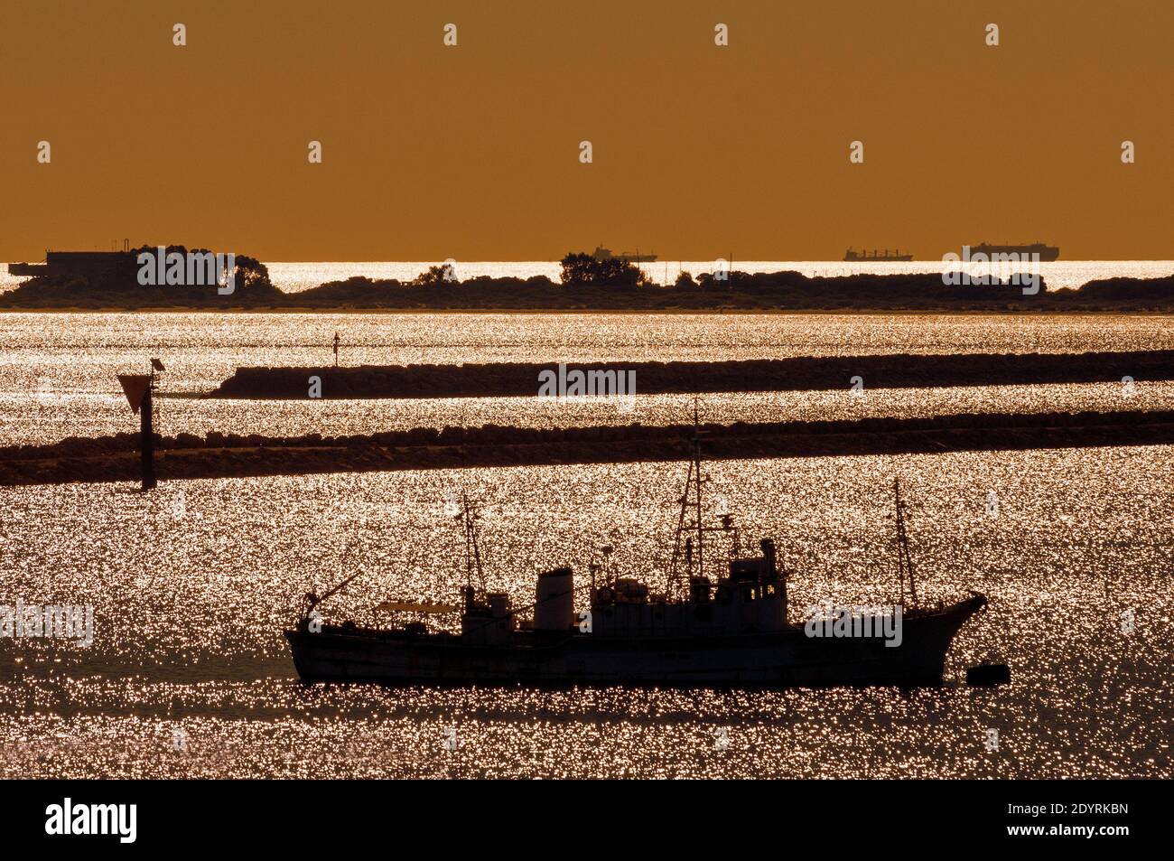 Eine nautische Szene mit einer tiefen Sonne, die von der Ozeane reflektiert wird und Schiffe silhouettiert. Stockfoto