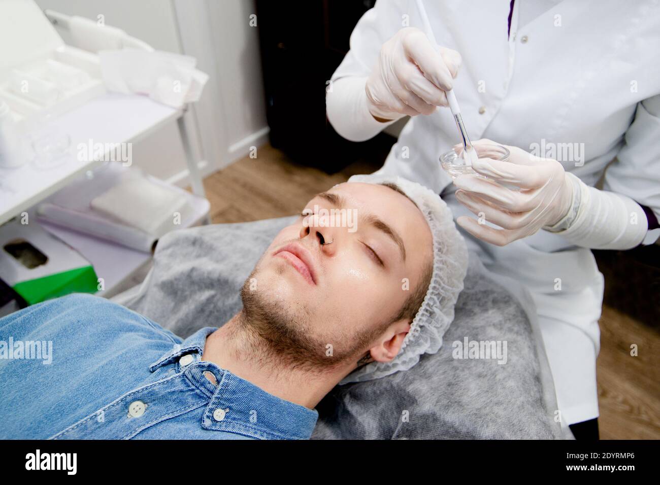 Der Kosmetologe hebt das Gesicht des jungen Mannes an Der Schönheitssalon Stockfoto