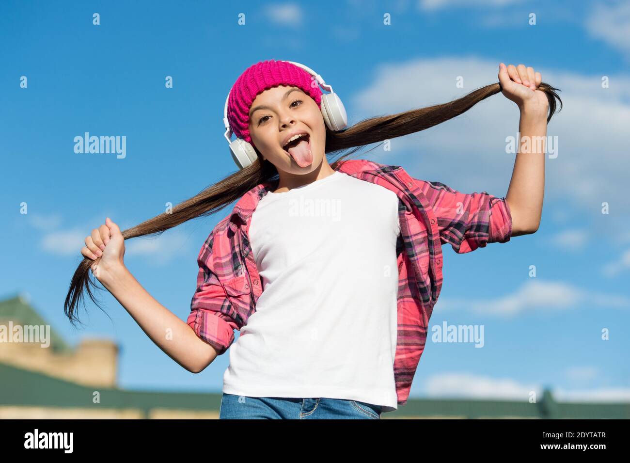 Lustige Mädchen Stick aus Zunge hören Musik und halten lange Brünette Haare sonnigen Himmel, Haarpflege. Stockfoto