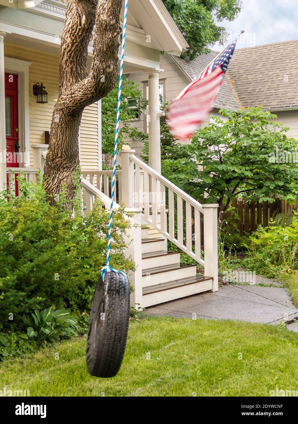 Wind aus vorbeiziehenden Gewitter bläst die amerikanische Flagge und die Reifenschaukel im Vorgarten dieses Kolonialhauses - Metapher für die Bedrohung der Demokratie Stockfoto