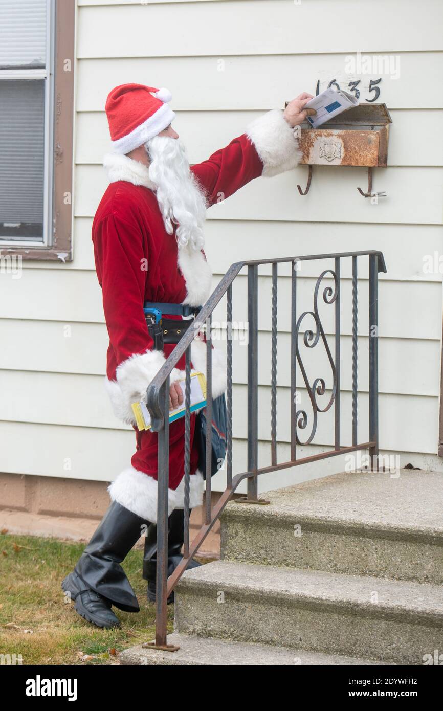 Winneconne, WI – 23. Dezember 2020: Ein Postdienst der USPS ist als Weihnachtsmann verkleidet, als er Post an ein Haus liefert. Stockfoto