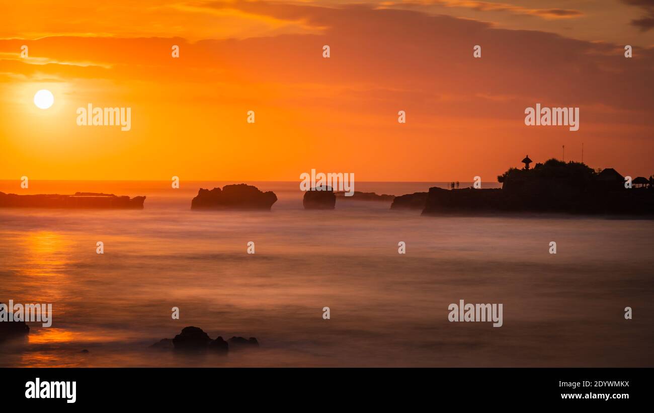 bali spirituelles Licht bei Sonnenuntergang am Strand farbenfroher Himmel Und ruhiges Wasser mit hindu-Tempel in der Ferne Stockfoto