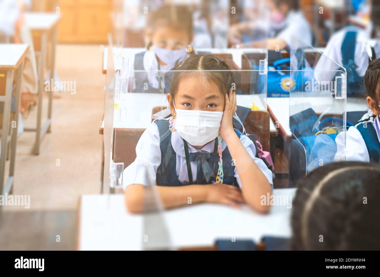 Asiatische Grundschule in Uniform sitzen im Klassenzimmer, trägt medizinische Maske während des Studiums, Plastikschild auf Schüler Schreibtisch, Schutz Schüler in der Klasse Stockfoto