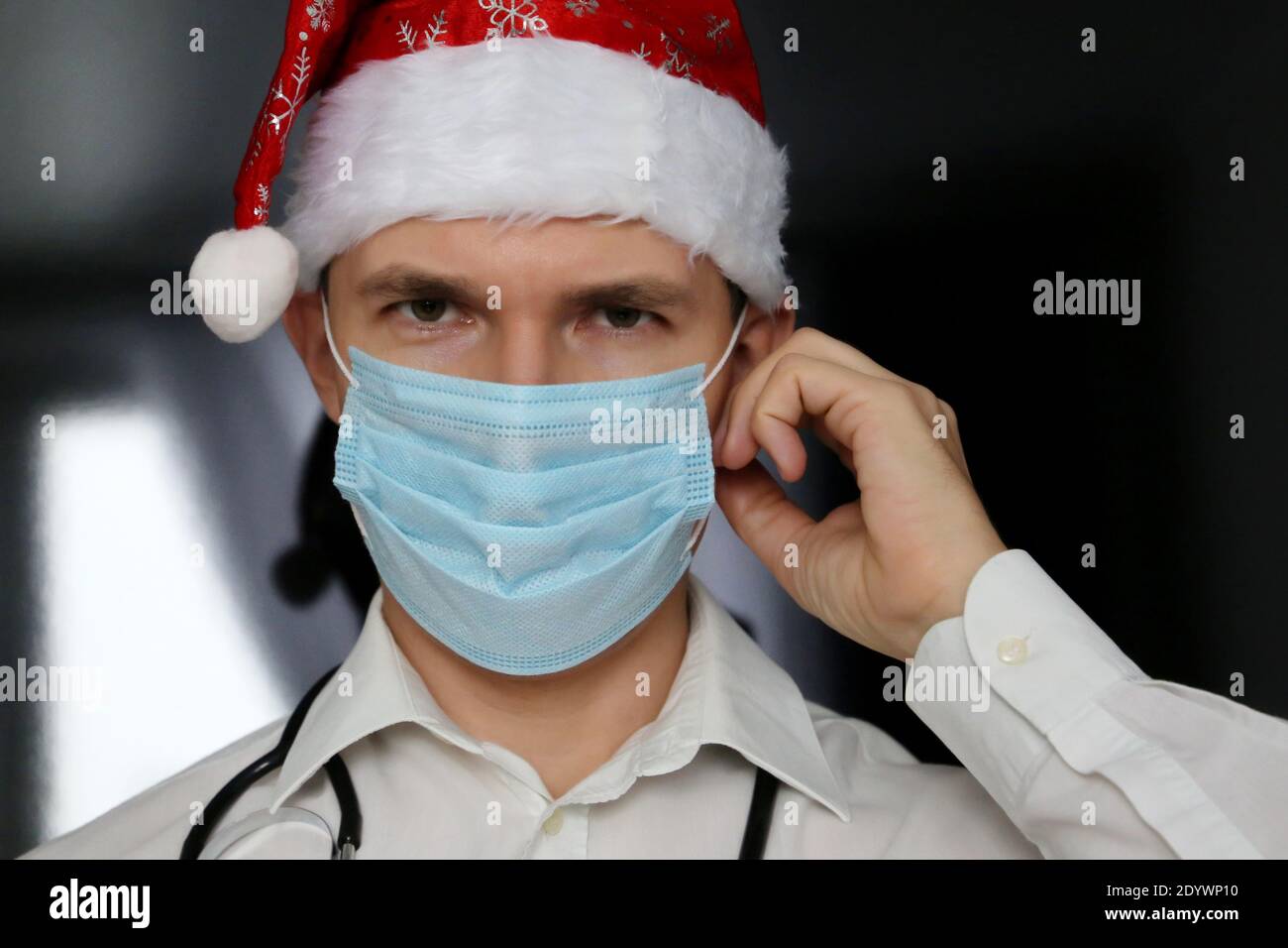 Porträt eines Arztes in medizinischer Gesichtsmaske und Weihnachtsmannhut. Neujahrsfeier in der Klinik während der Coronavirus-Pandemie Stockfoto