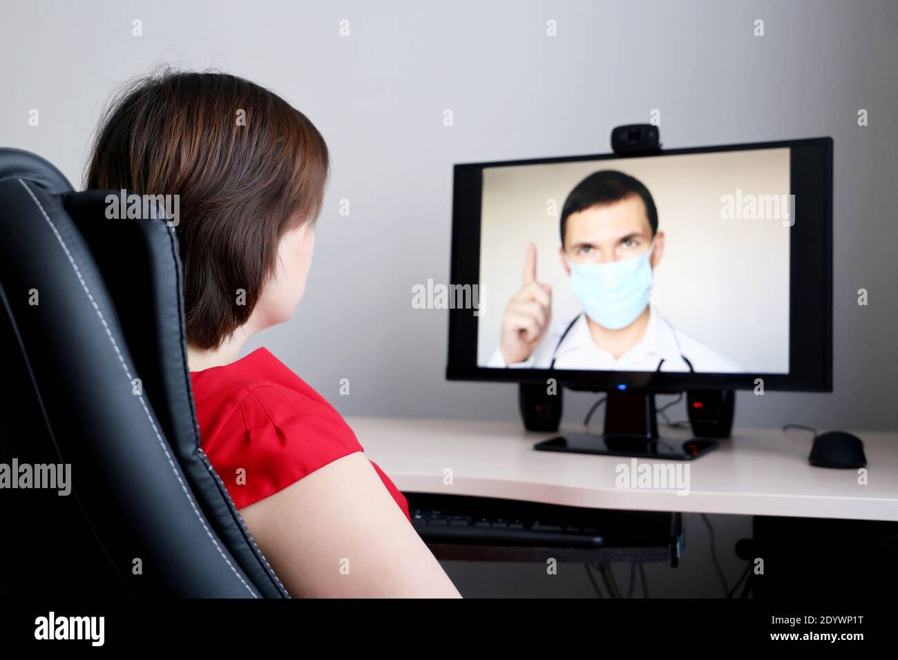 Online-Beratung mit einem Arzt, Frau hört sich die Arztempfehlungen sitzen vor der PC-Webcam. Mann in medizinischer Maske auf dem Display Stockfoto