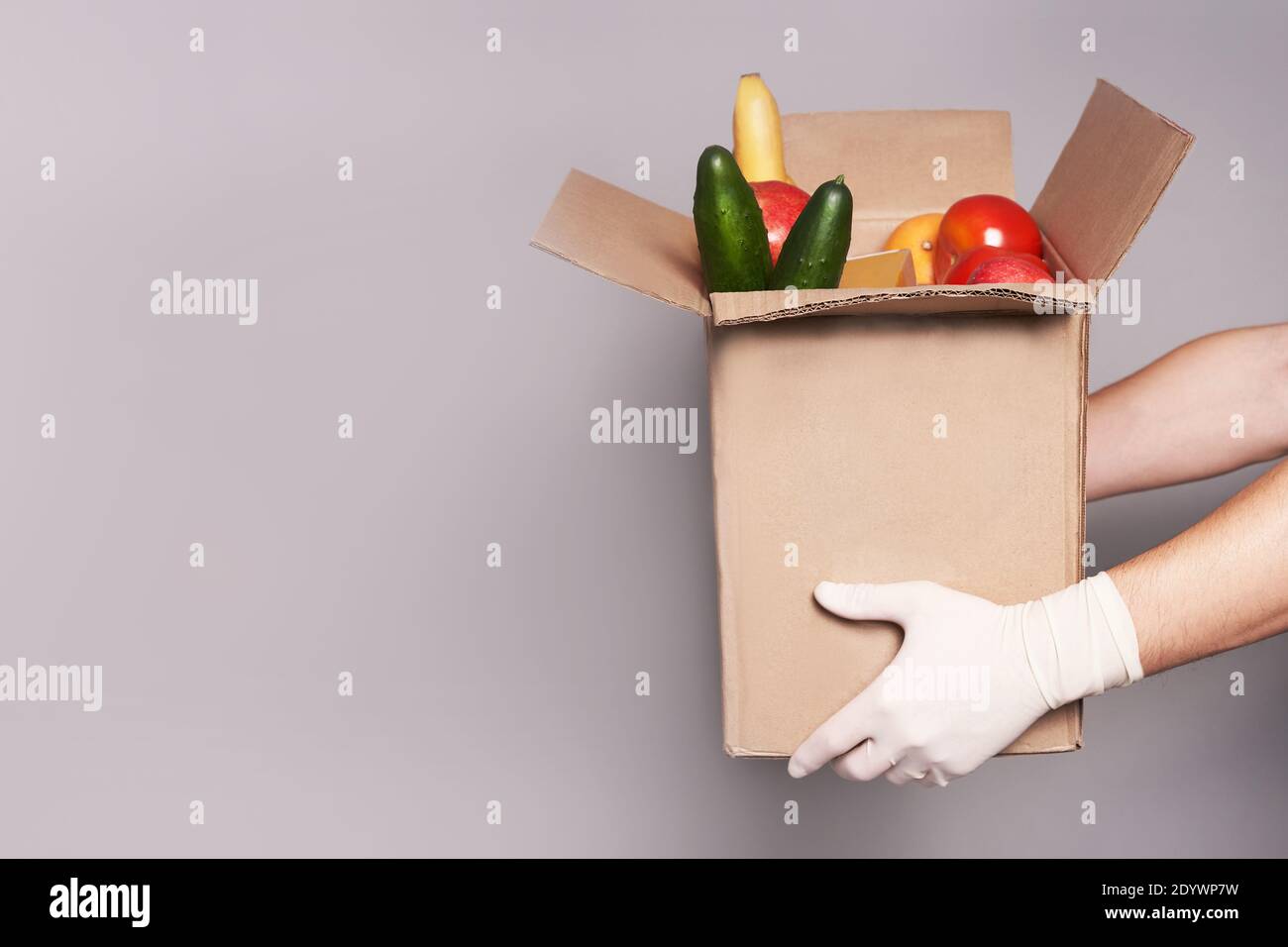 Hände von weißen Kurier in Gummihandschuhen halten einen Karton mit Lebensmitteln, schnelle und sichere Lieferung von Lebensmitteln. Stockfoto