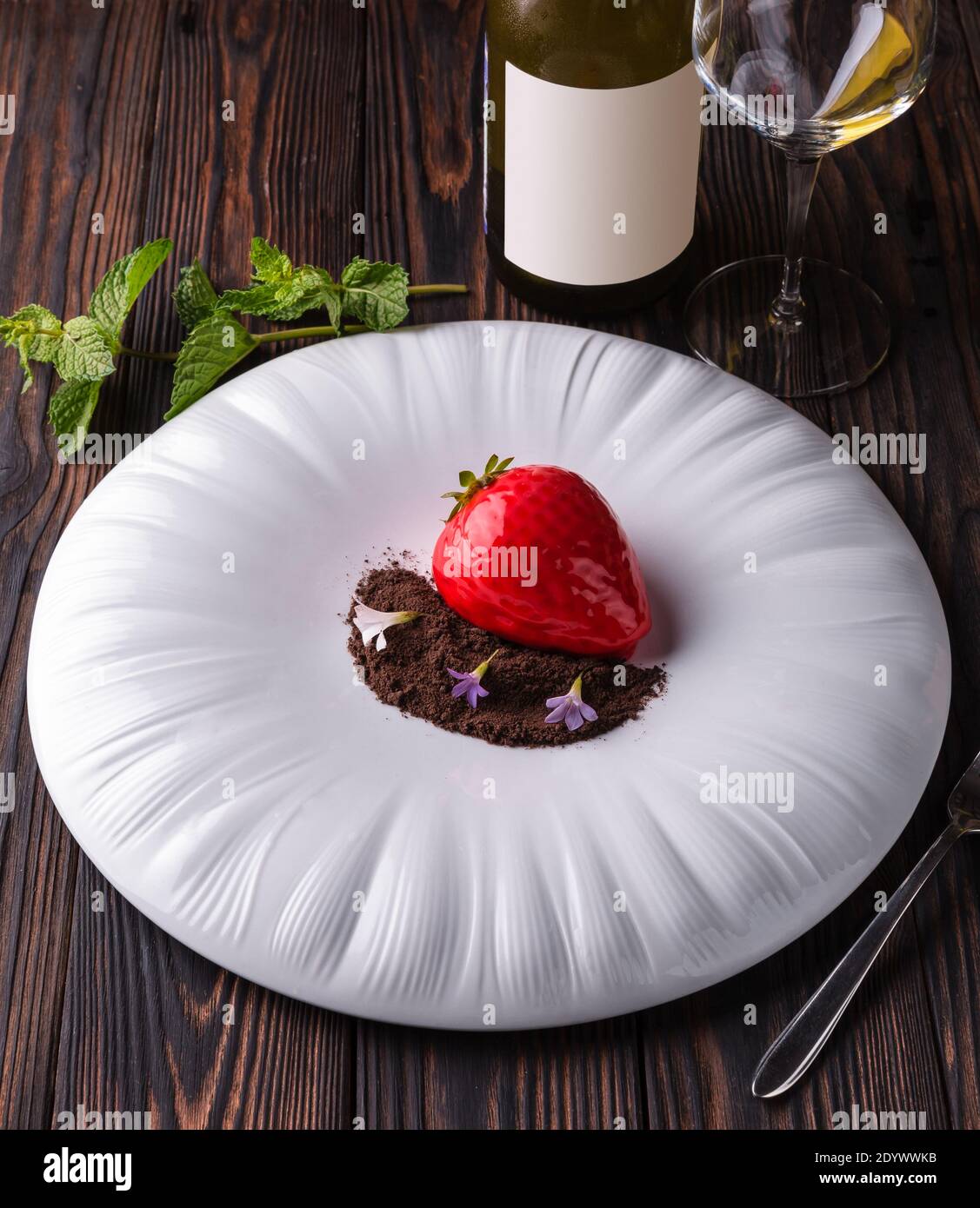 Rote Erdbeere Dessertkuchen mit Schokoladenstückchen und Veilchen auf einem großen weißen Teller. Stockfoto