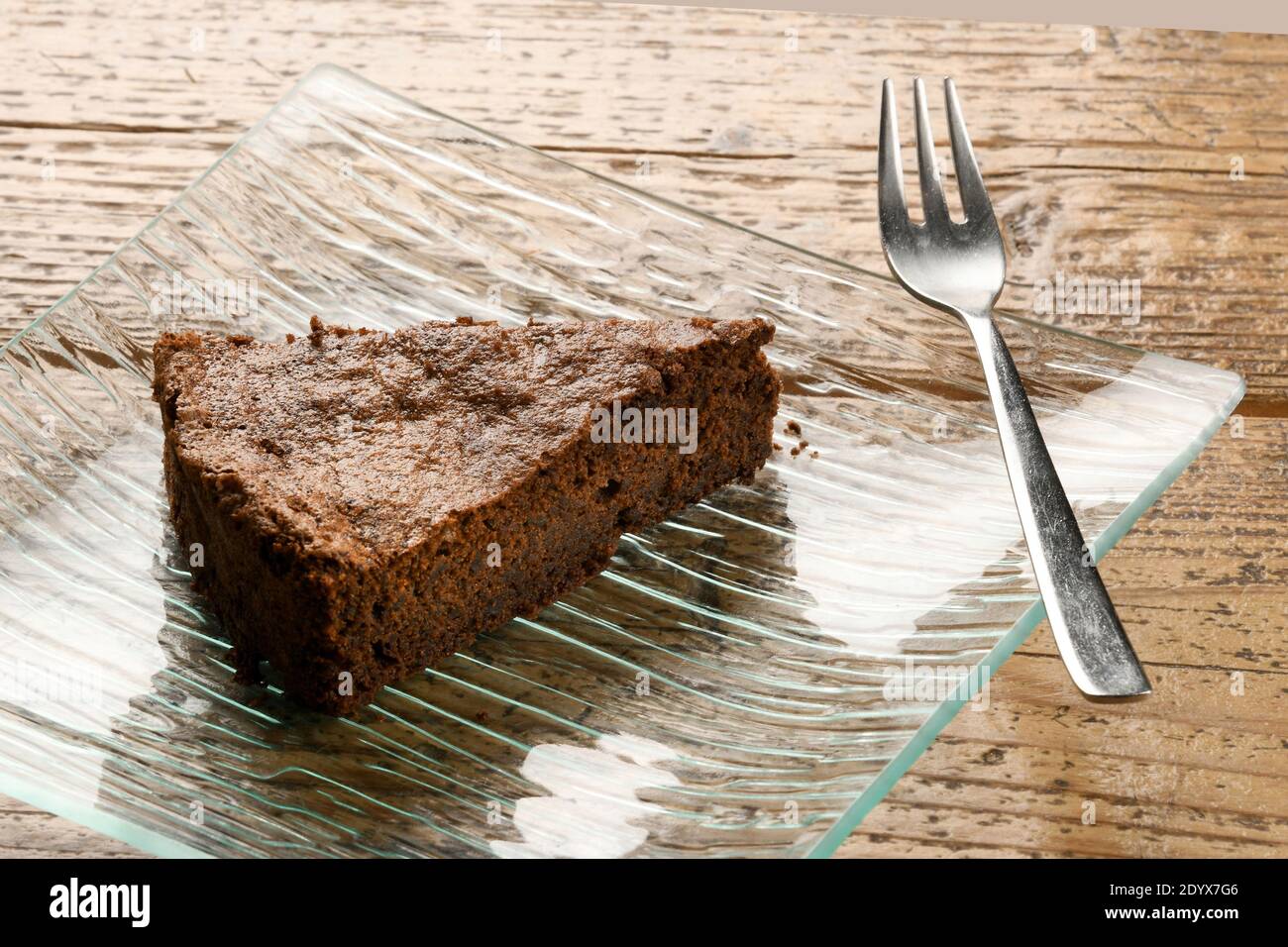 Eine Scheibe frisch gebackenen Schokoladenkuchen auf einem serviert Stilvolle rechteckige Glasschale mit Gabel auf einem Holztisch In einem hohen Winkel Stockfoto