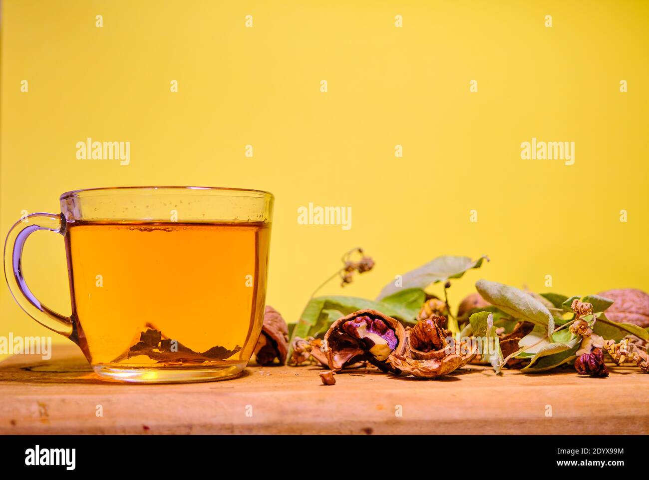 Foto von Kräuter- und Lindentee in der Glaskanne zusammen mit Lindenteeblättern und gebrochenen und nicht gebrochenen Walnüssen auf dem Holztisch. Stockfoto