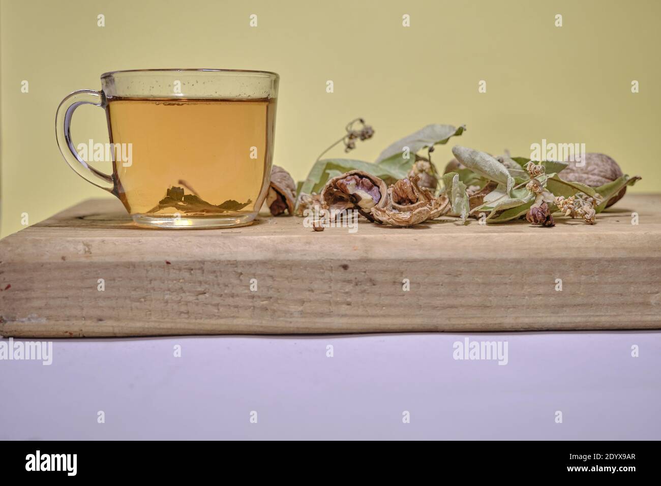 Foto von Kräuter- und Lindentee in der Glaskanne zusammen mit Lindenteeblättern und gebrochenen und nicht gebrochenen Walnüssen auf dem Holztisch. Stockfoto