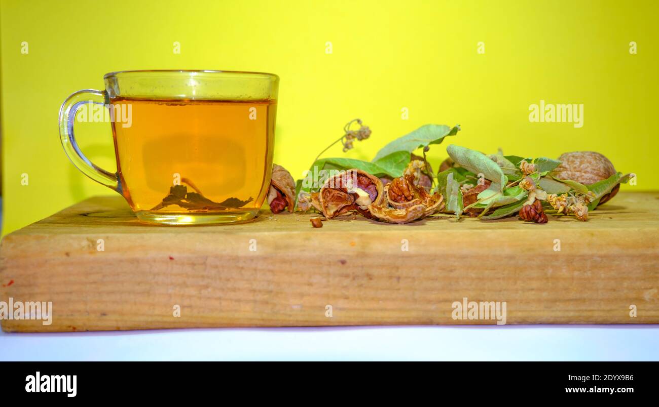 Foto von Kräuter- und Lindentee in der Glaskanne zusammen mit Lindenteeblättern und gebrochenen und nicht gebrochenen Walnüssen auf dem Holztisch. Stockfoto