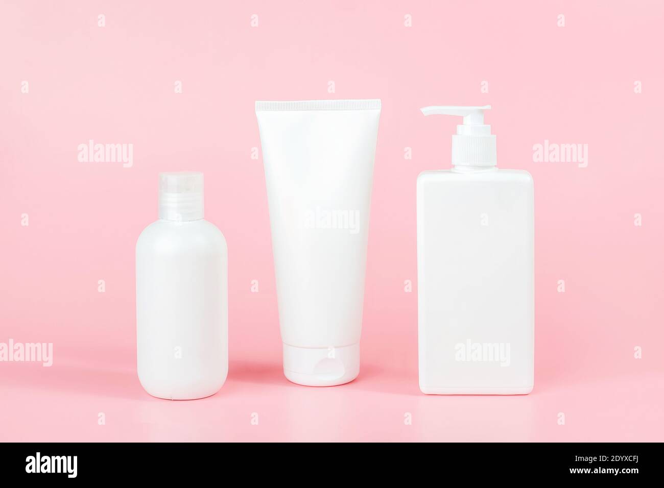 Pflegekosmetikset für Haut, Körper oder Haar. Drei weiße leere Kosmetikflaschen, Tube auf rosa Hintergrund. Spa Kosmetikkonzept. Vorderansicht MOC Stockfoto