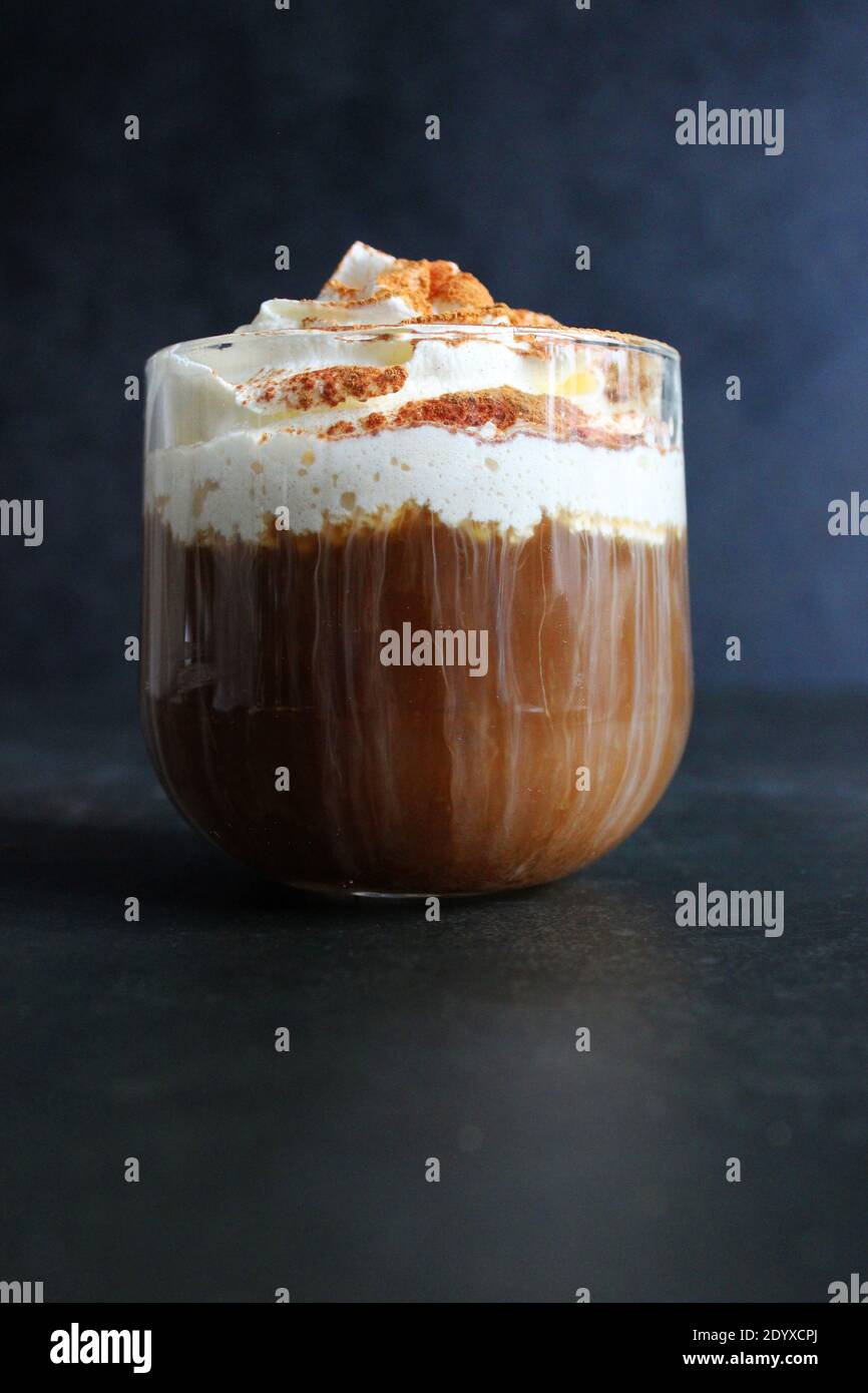 Schaumig Kaffee trinken. Cappuccino oder Latte in einem transparenten Glas auf dunklem Grund Stockfoto