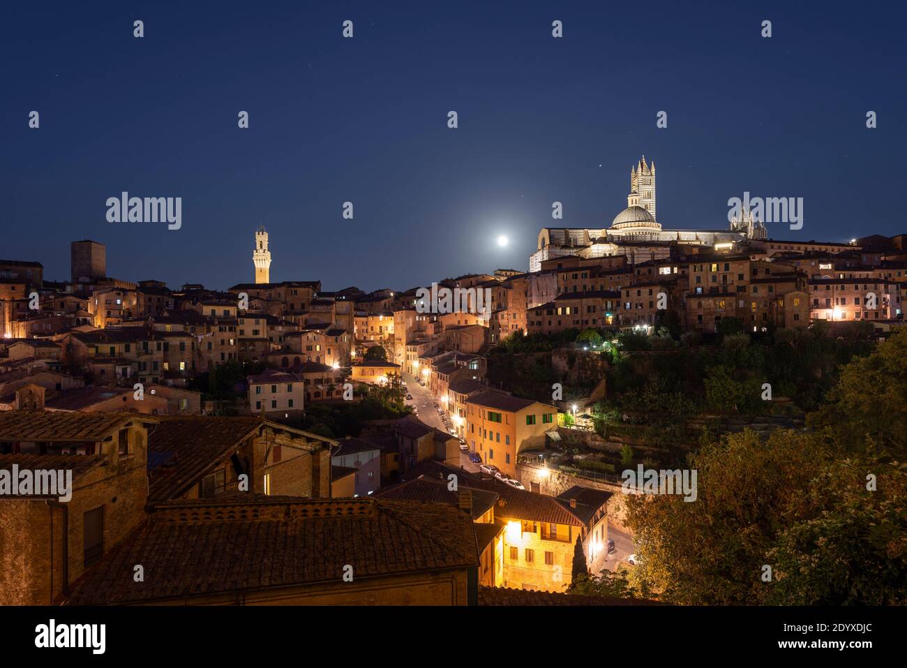 Vollmond über einer beleuchteten Gasse und das Panorama der mittelalterlichen Altstadt von Siena mit der Kathedrale, Rathaus Uhrenturm, Toskana, Italien Stockfoto
