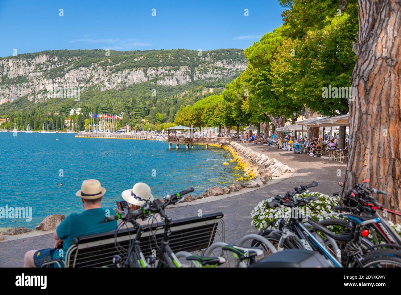 Blick auf Mann und Frau in Hüten mit Blick auf Promenade und See an einem sonnigen Tag, Garda, Gardasee, Provinz Verona, Italien, Europa Stockfoto