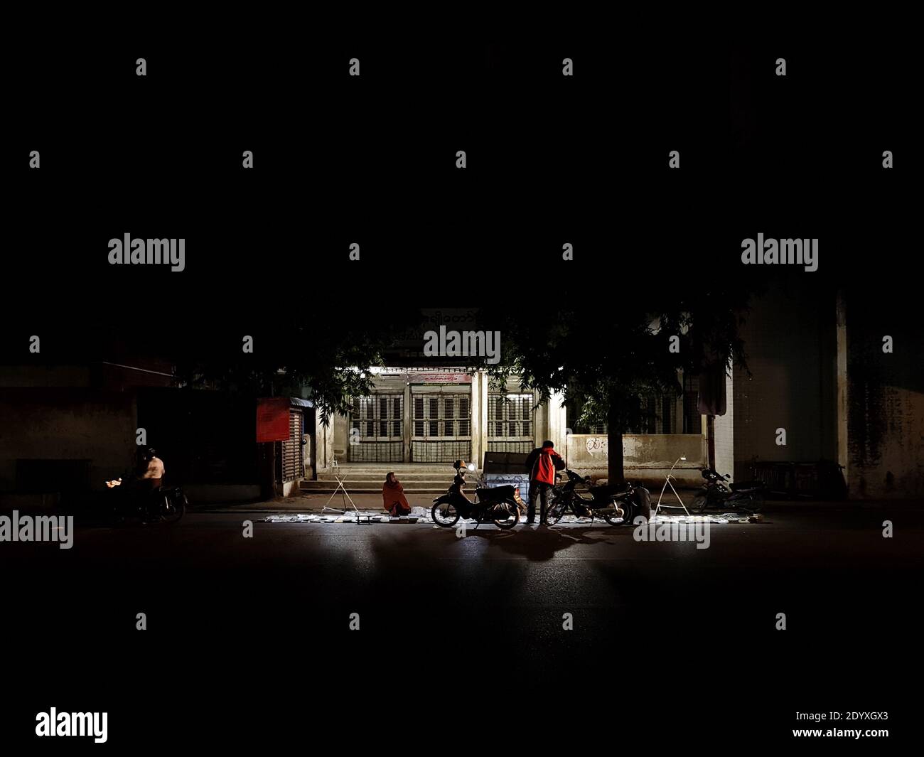 Mandalay, Myanmar - der Straßenhändler und der Mann, der sich spät in der Nacht um Dinge umsah. Szene von einsamen Hinterstraße. Stockfoto