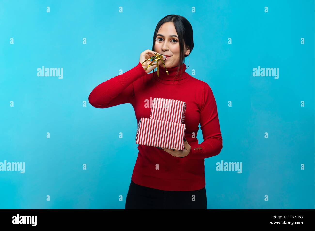 Junge Frau weht Party Horn trägt roten Sweatshirt und halten Geschenkbox in der Hand Stockfoto