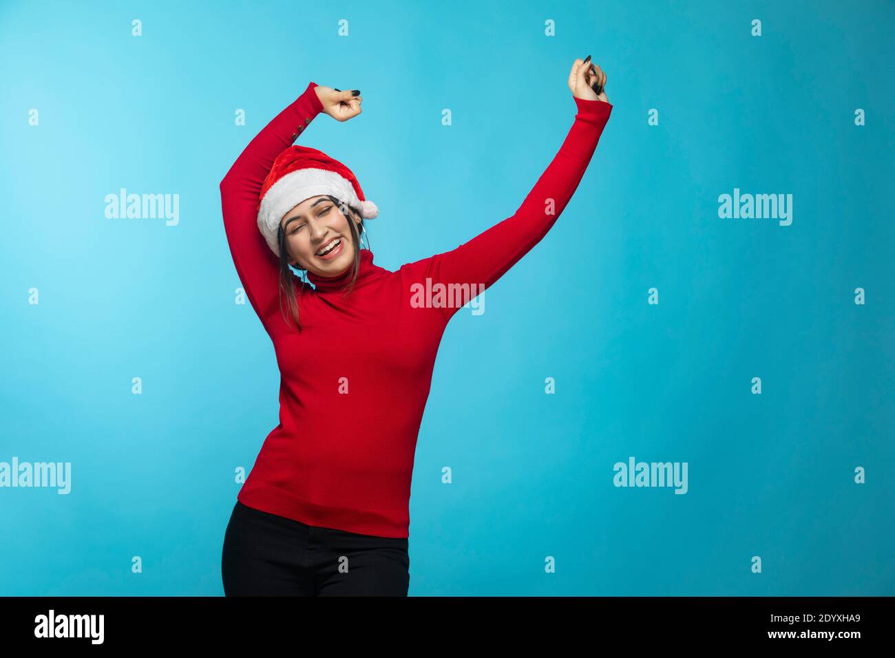 Glücklich aufgeregt junge Frau in weihnachtsmann Hut tanzen und Lachend über blauem Hintergrund Stockfoto