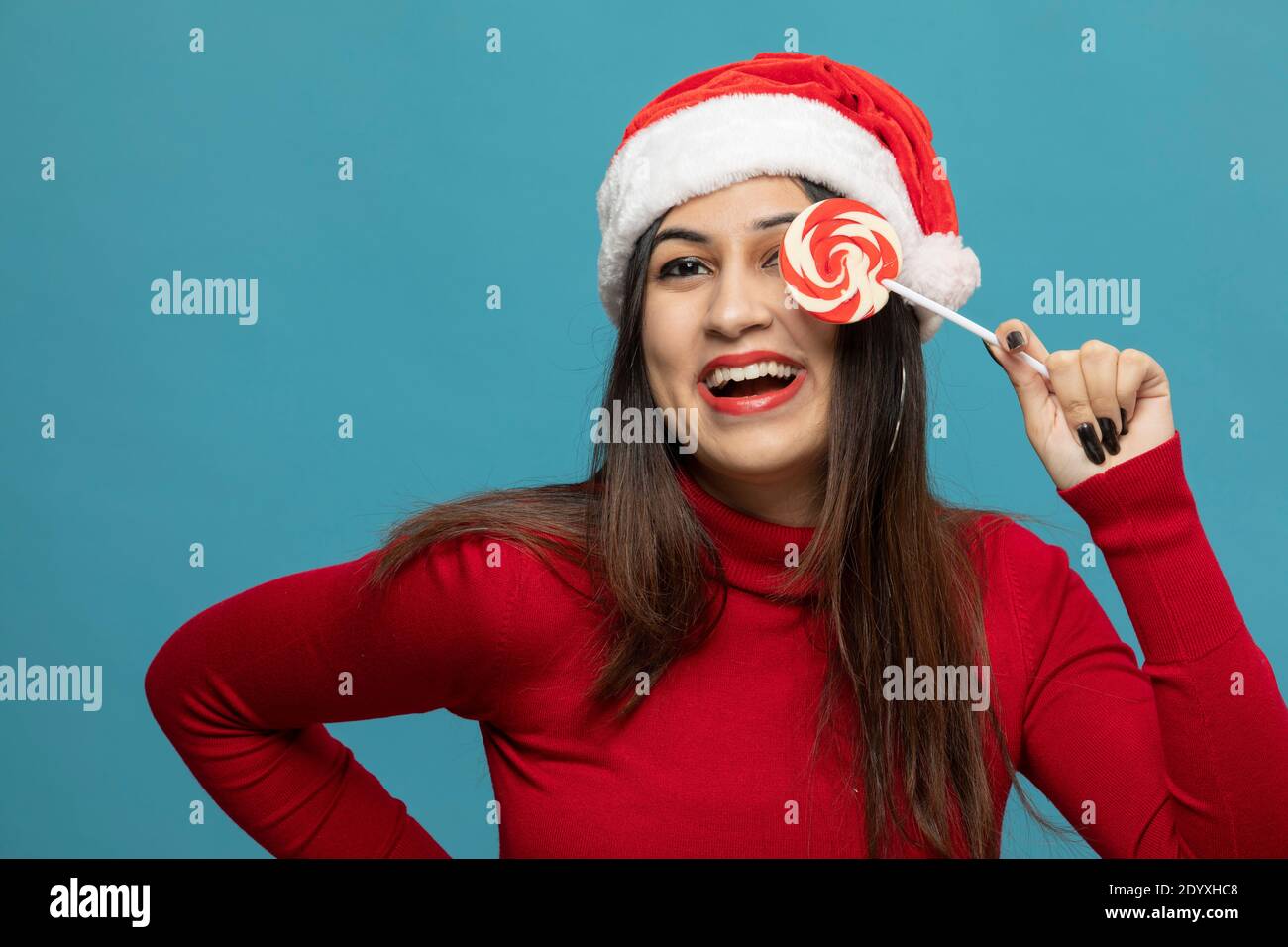 Junge Frau trägt Weihnachtsmann Hut über ein Auge mit Lollipop Und lächelnd Stockfoto