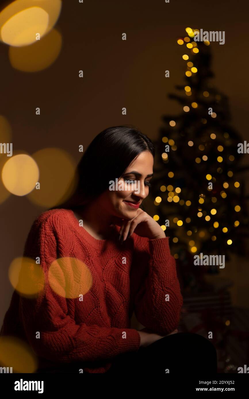 Lächelnde Frau Sitzt Zu Hause In Der Nähe Von Weihnachtsbaum Stockfoto