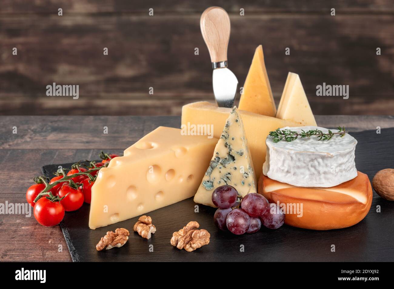 Verschiedene Sorten Käse mit Walnüssen und Trauben auf schwarzem Schiefertafel auf rustikalem Holzhintergrund. Blauschimmelkäse Dorblin, geräucherte Suluguni, Brie, Maasdam, c Stockfoto