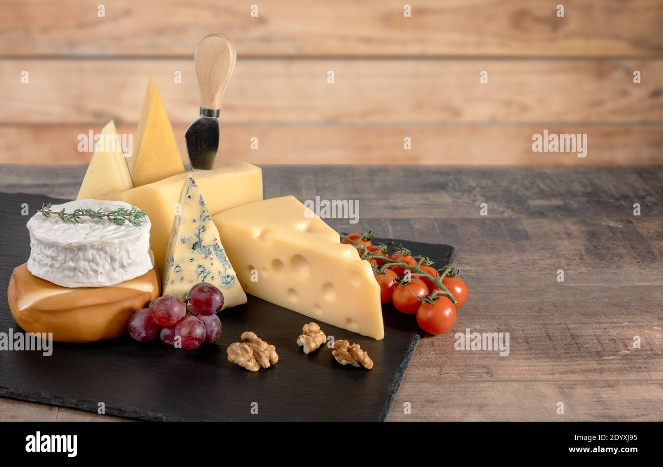 Verschiedene Sorten Käse mit Walnüssen und Trauben auf rustikalem Holzhintergrund. Blauschimmelkäse Dorblin, geräucherter Suluguni, Brie, Maasdam, Cheddar, Parmesan.Asso Stockfoto