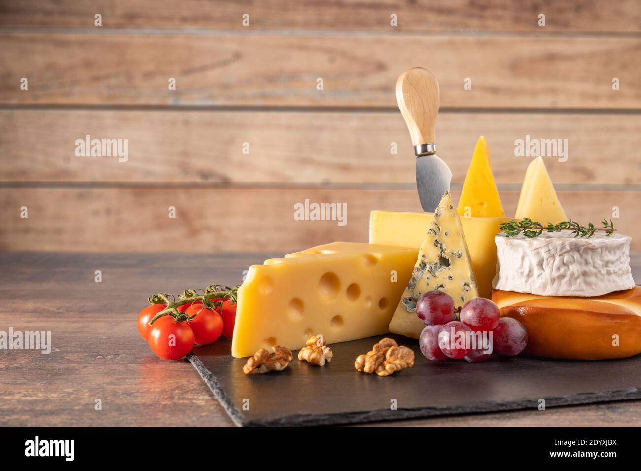 Verschiedene Käsesorten auf rustikalem Holztisch. Käseplatte: Parmesan, Cheddar, gouda, Camembert, Brie mit Nüssen auf Holzbrett auf dunklem Hintergrund w Stockfoto