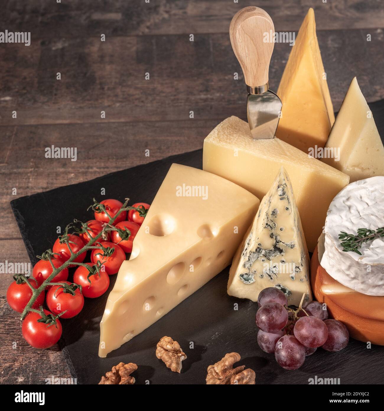 Verschiedene Käsesorten auf rustikalem Holztisch. Käseplatte: Parmesan, Cheddar, gouda, Camembert, Brie mit Nüssen auf Holzbrett auf dunklem Hintergrund w Stockfoto