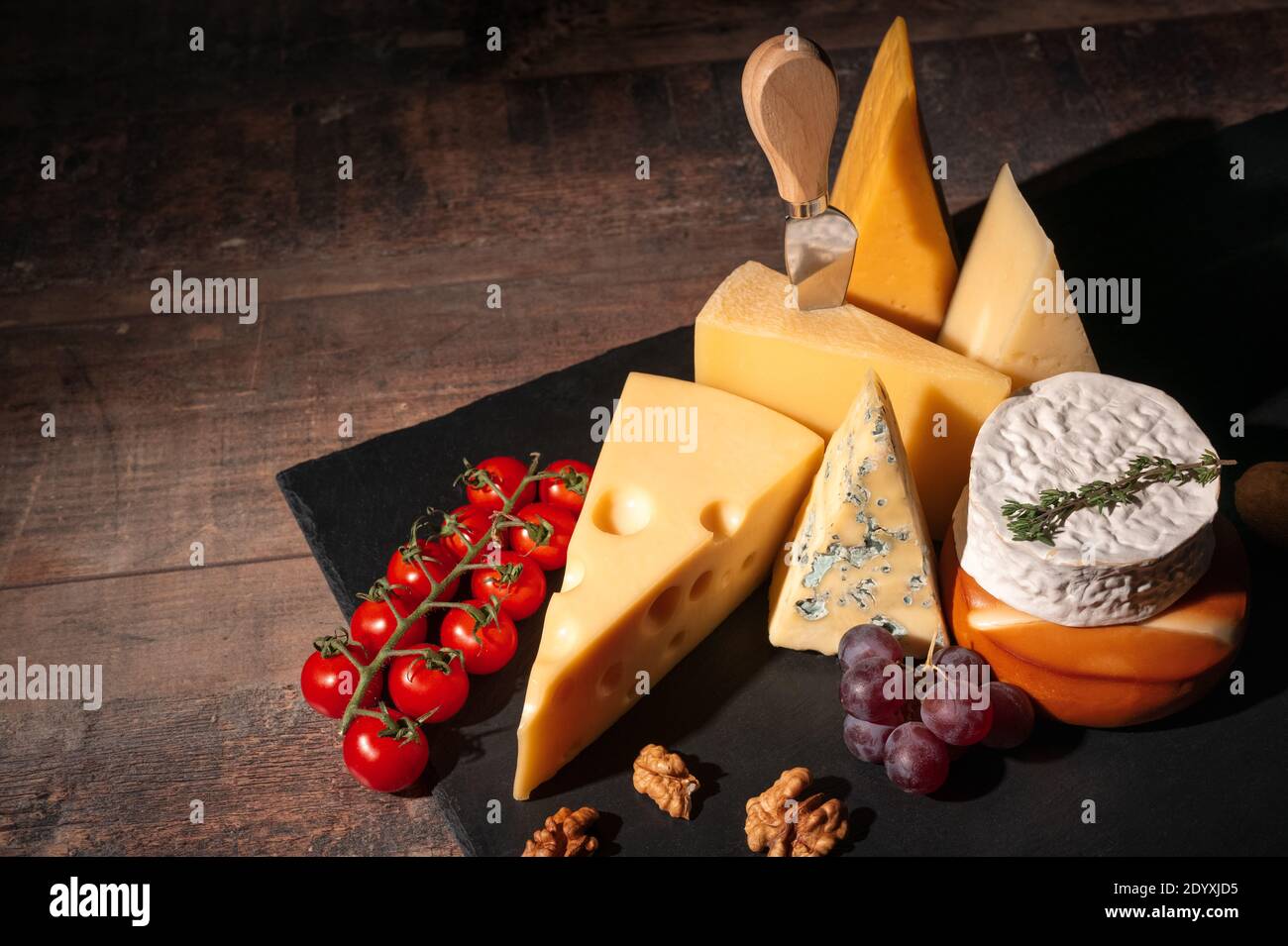 Verschiedene Käsesorten auf rustikalem Holztisch. Käseplatte: Parmesan, Cheddar, gouda, Camembert, Brie mit Nüssen auf Holzbrett auf dunklem Hintergrund w Stockfoto