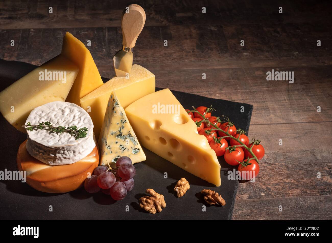 Verschiedene Käsesorten auf rustikalem Holztisch. Käseplatte: Parmesan, Cheddar, gouda, Camembert, Brie mit Nüssen auf Holzbrett auf dunklem Hintergrund w Stockfoto