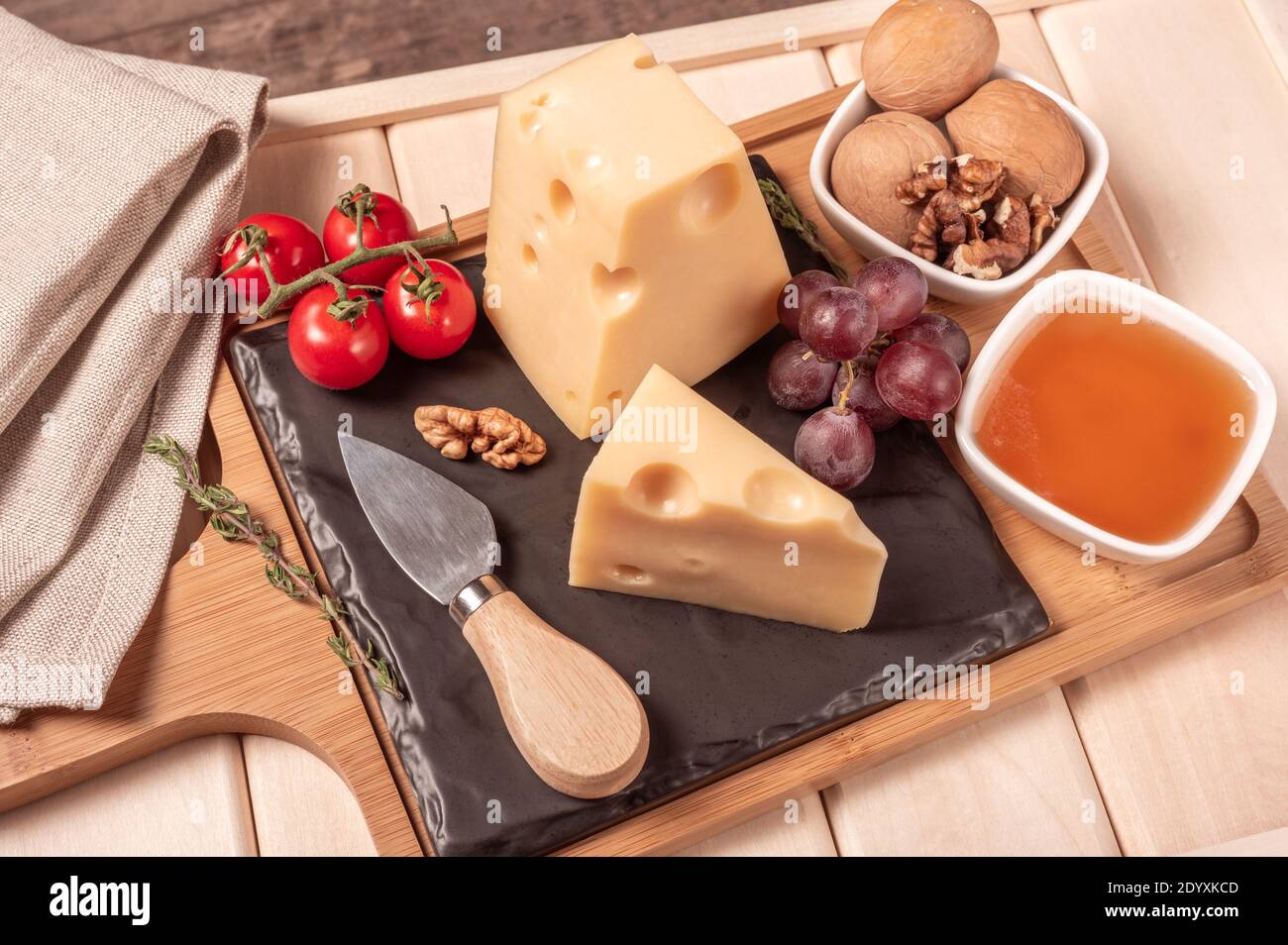 Käse maasdam mit Nüssen, Honig, Trauben und Tomaten auf Holzbrett und Tablett. Käse Dessert. Getöntes Bild Stockfoto
