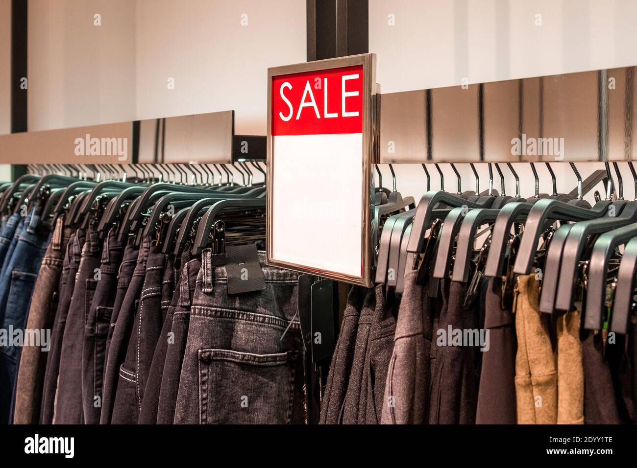 Rote Platte mit Informationen über den Verkauf ist über den Kleiderbügeln mit Hosen in einem Bekleidungsgeschäft. Promotion, Werbung, Shopping und Black friday Conce Stockfoto