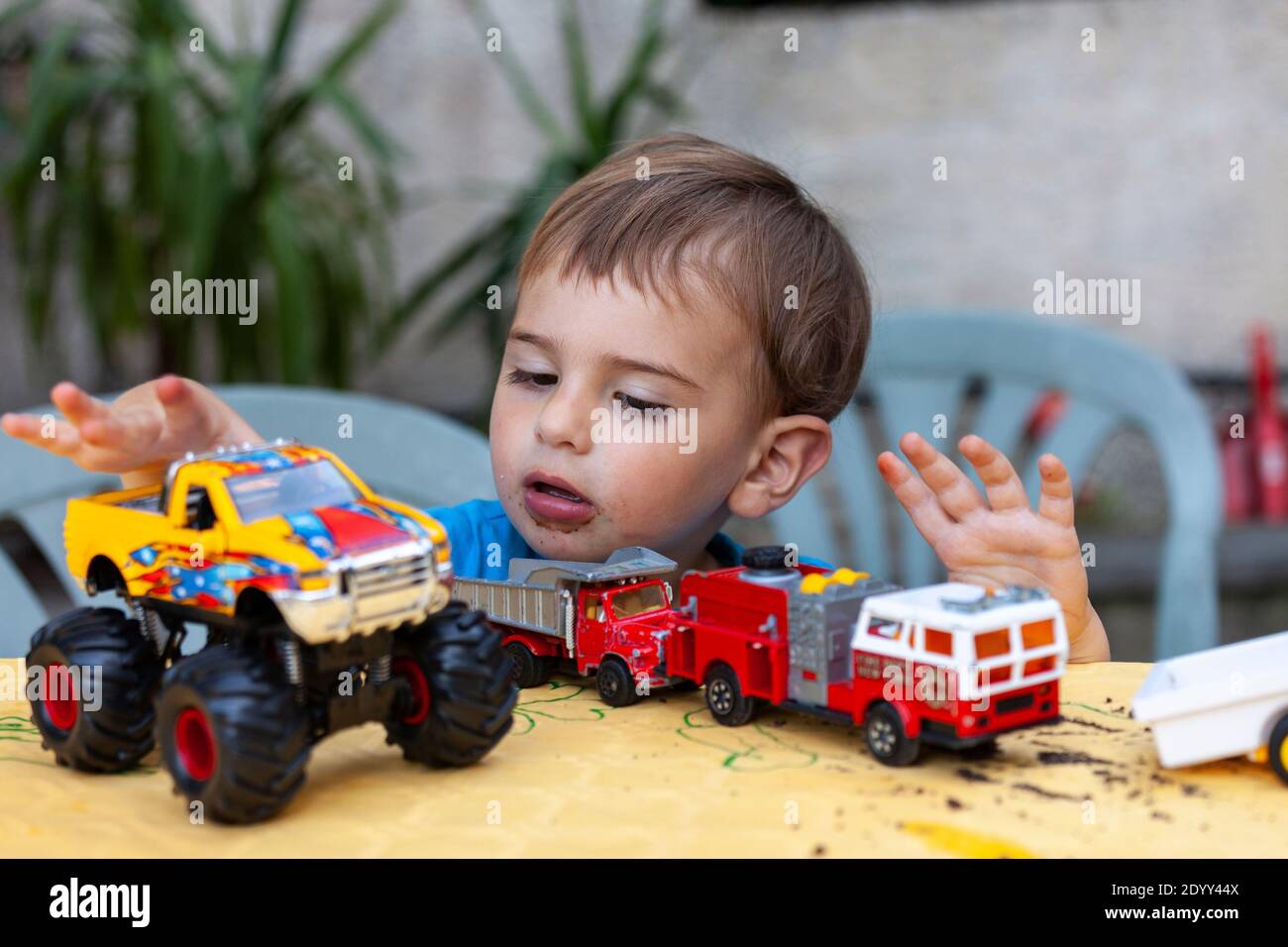 Ein Kind spielt mit seinem neuen Spielzeug, einem Feuerwehrauto, einem Monstertruck und einem Lastwagen. Stockfoto