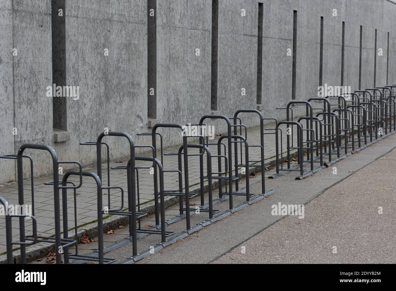 Lange Reihe leerer Fahrradständer neben dem Bürgersteig in der Nähe Geschlossene öffentliche Schule mit trüben grauen conrete Wand im Winter weihnachten Schulferien Stockfoto