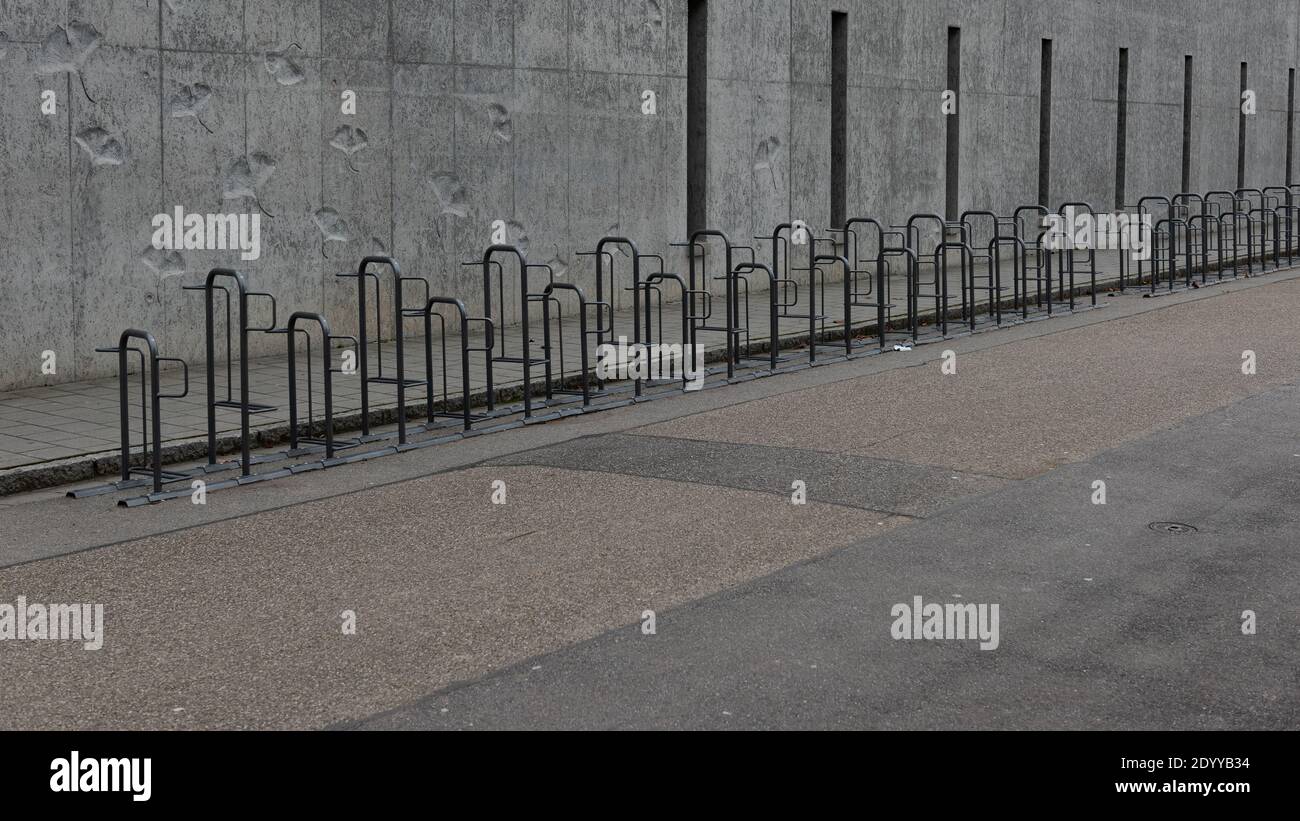 Lange Reihe leerer Fahrradständer neben dem Bürgersteig in der Nähe Geschlossene öffentliche Schule mit trüben grauen conrete Wand im Winter weihnachten Schulferien Stockfoto