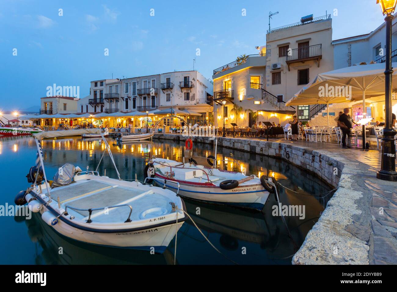 Boote und Tavernen am Wasser beleuchtet am Abend im alten venezianischen Hafen, Rethymno, Kreta, Griechenland Stockfoto